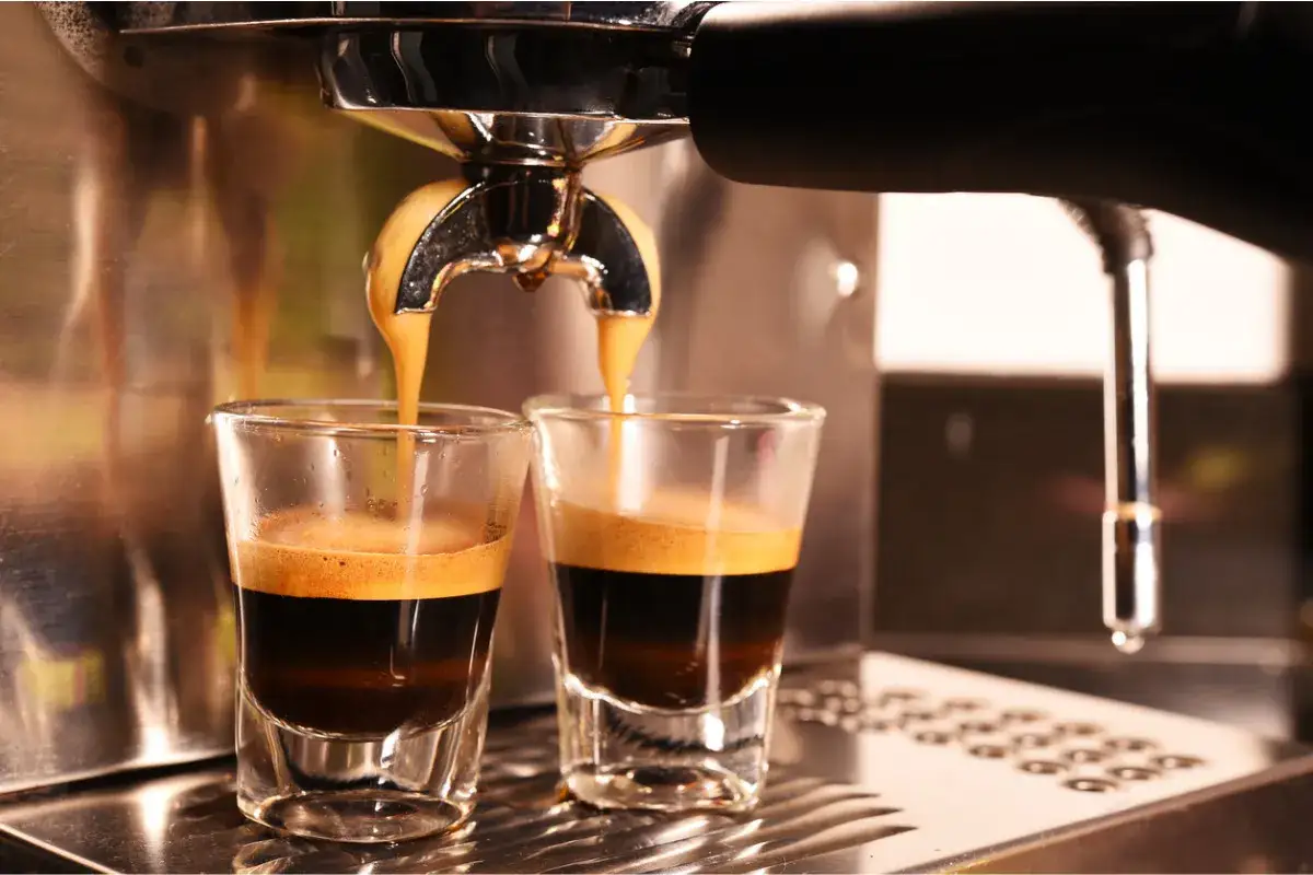 Zaparzanie dw&oacute;ch filiżanek espresso. Gorący nap&oacute;j z pianką spływa z ekspresu do małych szklanek.
