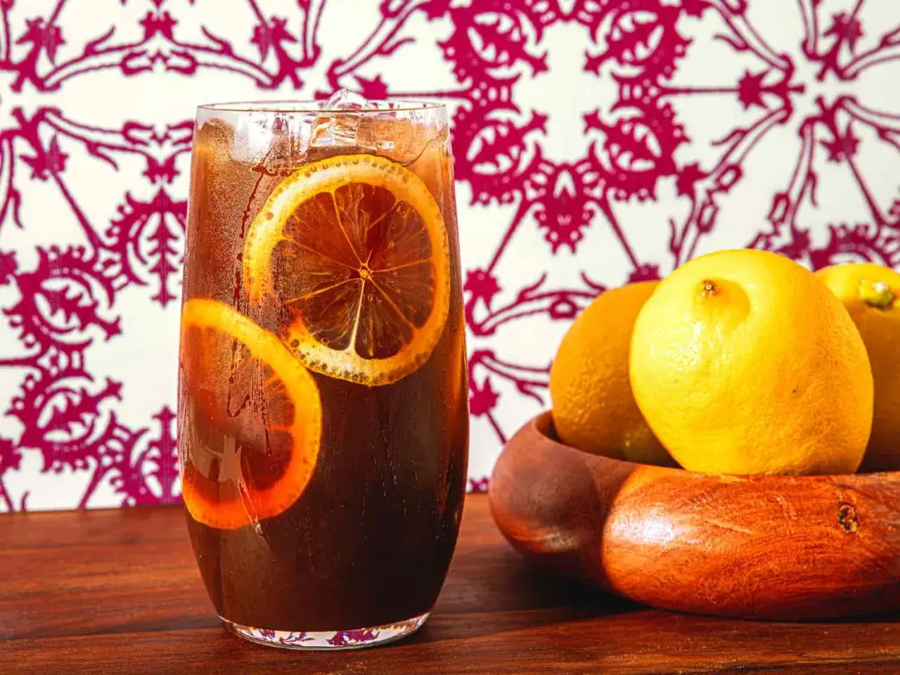 Erfrischender Eiskaffee italienisch mit Zitronenscheiben im Glas, daneben eine Schale mit Zitronen.
