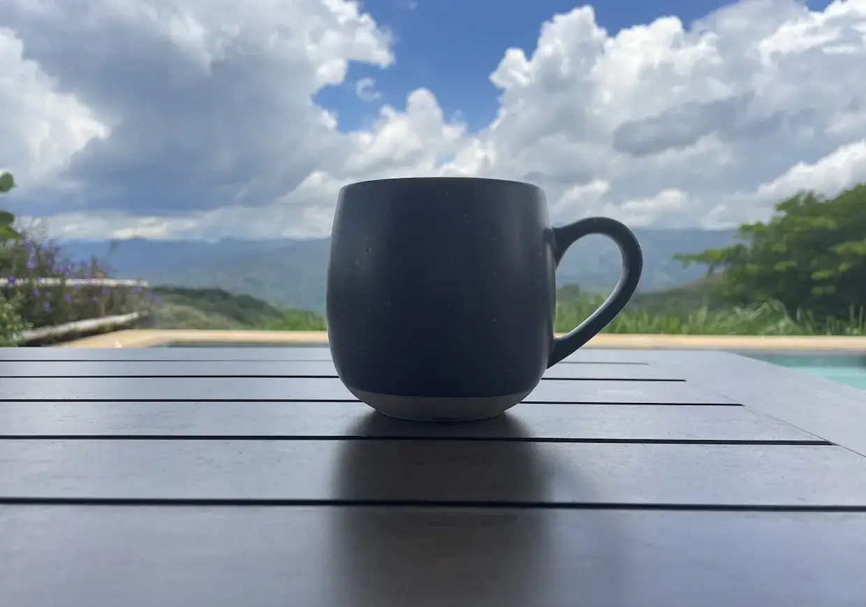 Dunkler Kaffee auf einem Tisch mit Blick auf Berge und Wolken. Ein gesunder Start in den Tag.