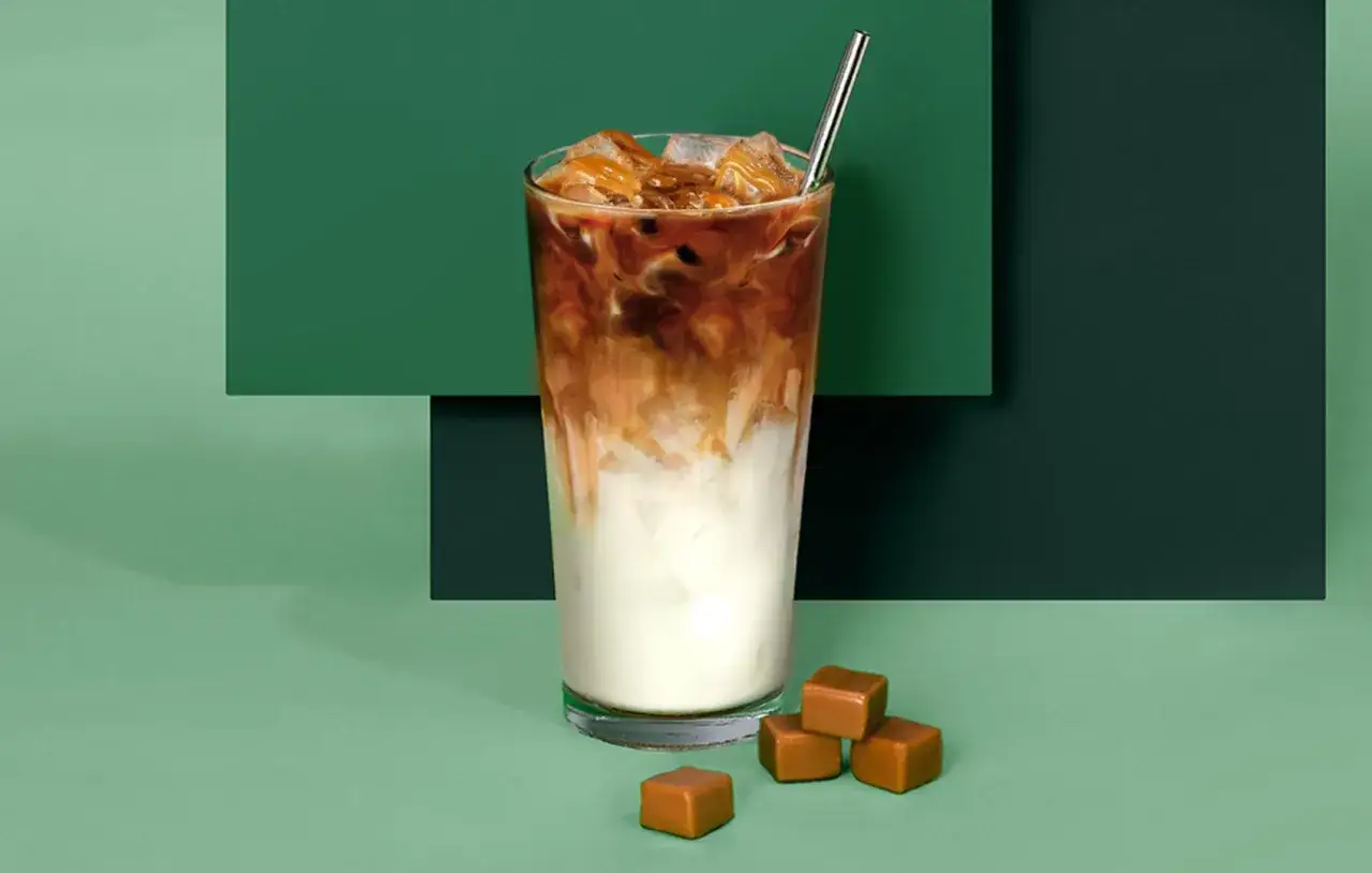 Ein erfrischender Iced Macchiato mit Karamell-Swirls und Eiswürfeln, daneben ein paar Karamellbonbons.