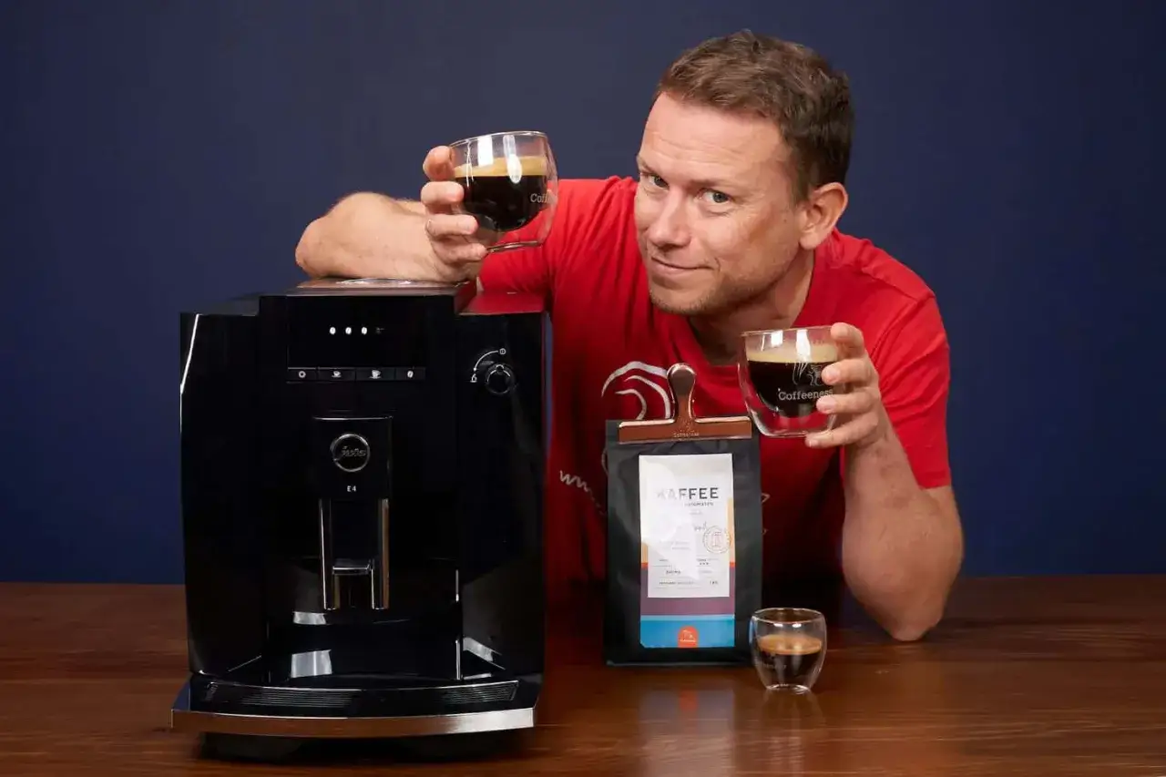 Mann h&auml;lt Kaffee hoch, neben Kaffeemaschine und Kaffeepackung. Er scheint zu denken: 