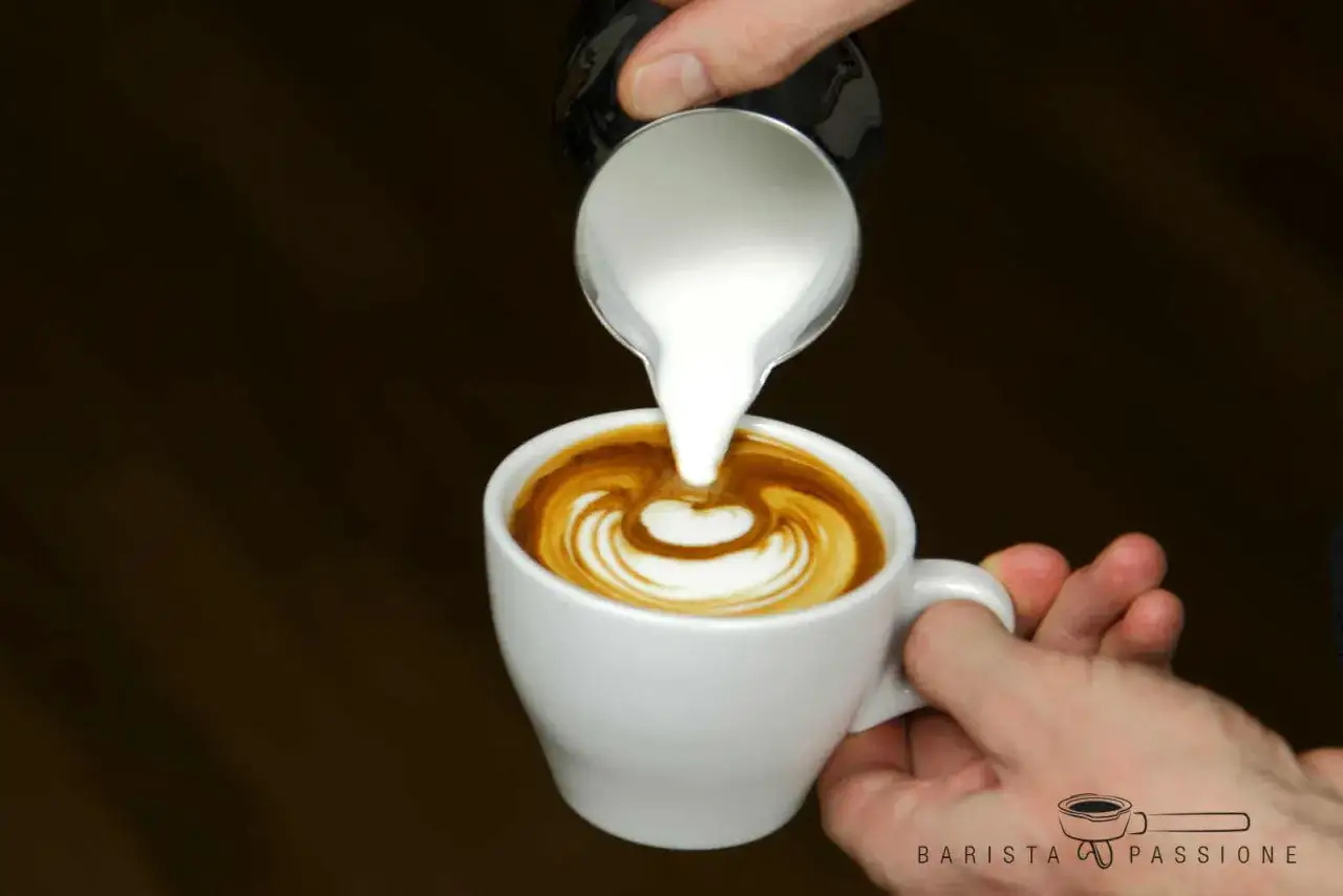 Barista gie&szlig;t Milchschaum in eine Tasse Kaffee, um ein Herzmuster zu kreieren. Perfekter Milchschaum zubereiten ist eine Kunst.