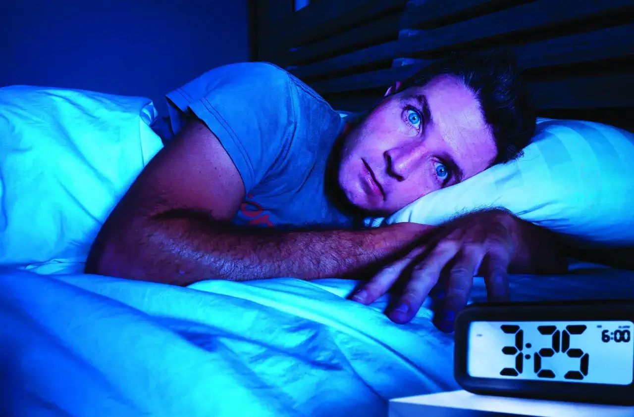Mann liegt wach im Bett, die Augen weit aufgerissen. Der Wecker zeigt 3:25 Uhr. Zu viel Koffein kann nicht schlafen, was tun?