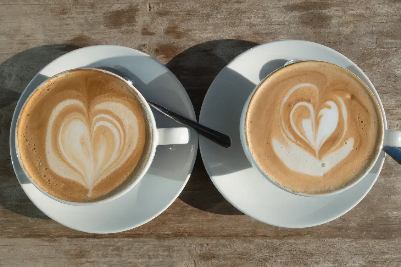 Zwei Kaffees mit Herz-Latte-Art auf Holztisch. Welcher ist der Flat White vs Cappuccino?