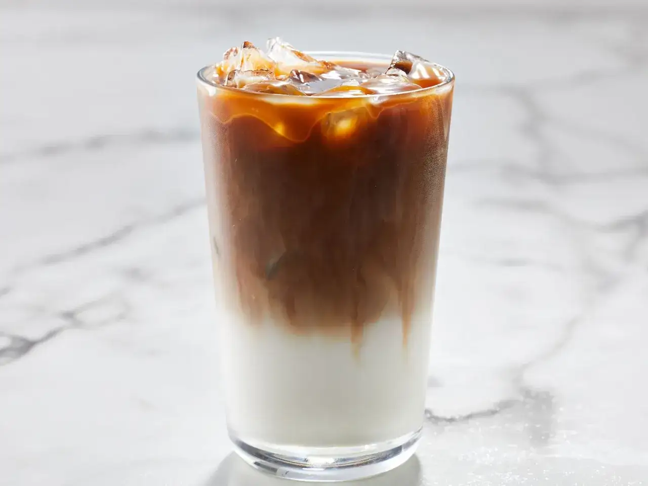 Ein erfrischender iced caramel macchiato mit geschichtetem Milchkaffee und Eiswürfeln auf Marmor.