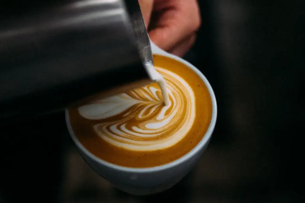 Barista verziert einen Oat Milk Latte mit kunstvollem Milchschaum-Muster.