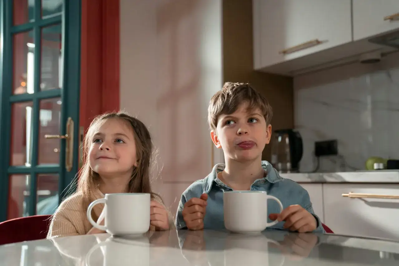 Zwei Kinder mit Tassen. Der Junge leckt sich die Lippen. Ab welchem Alter darf man Kaffee trinken?