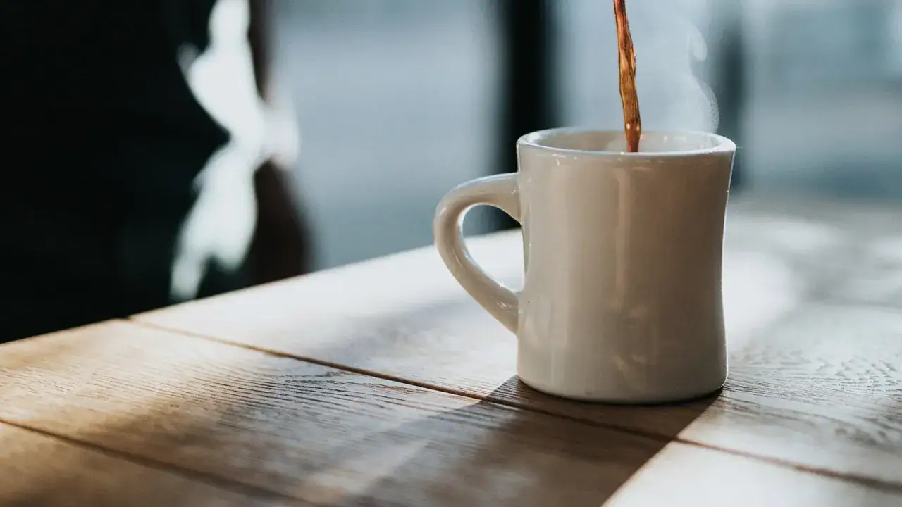 Heißer Kaffee wird in eine weiße Tasse gegossen, Dampf steigt auf. Ein Genuss, der die Vorteile von Kaffee für den Start in den Tag unterstreicht.