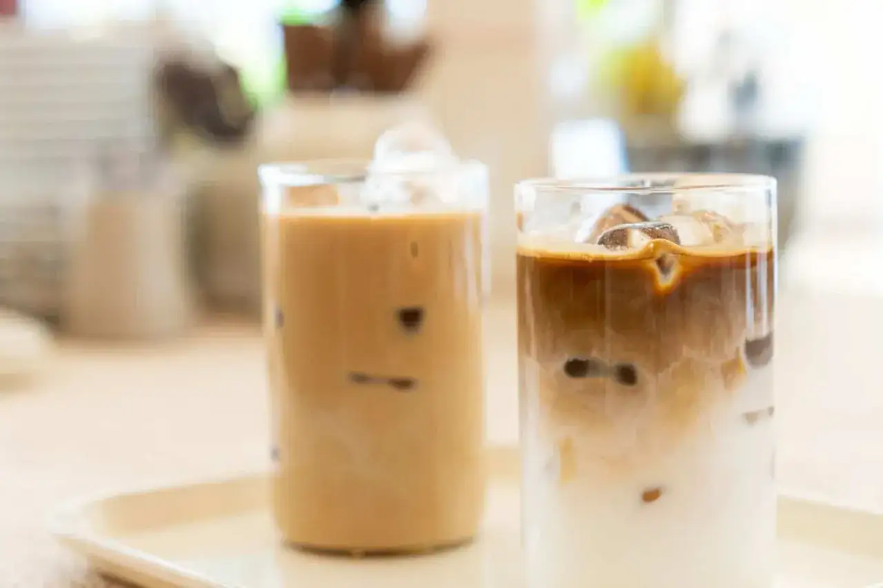 Zwei Gläser mit cremigem cafe helado, gefüllt mit Eiswürfeln und geschichtetem Kaffee und Milch.