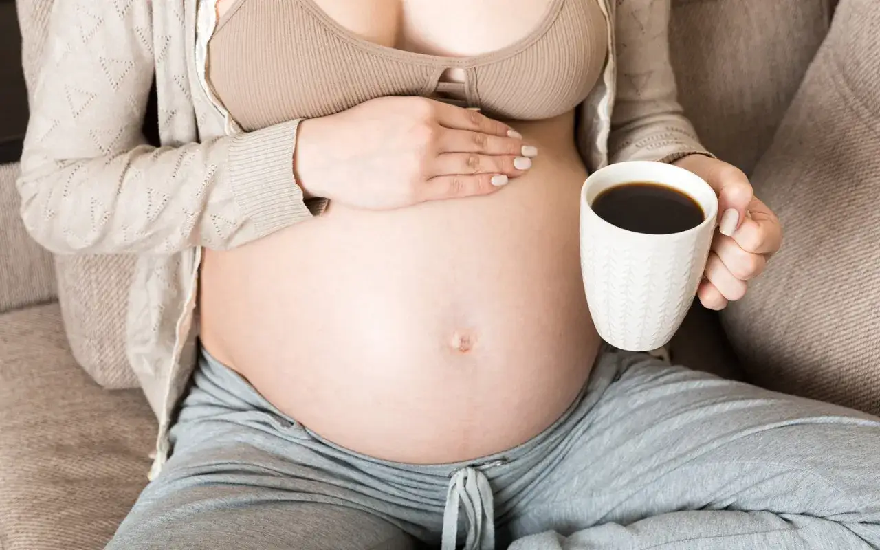 Schwanger und genießt eine Tasse Kaffee.