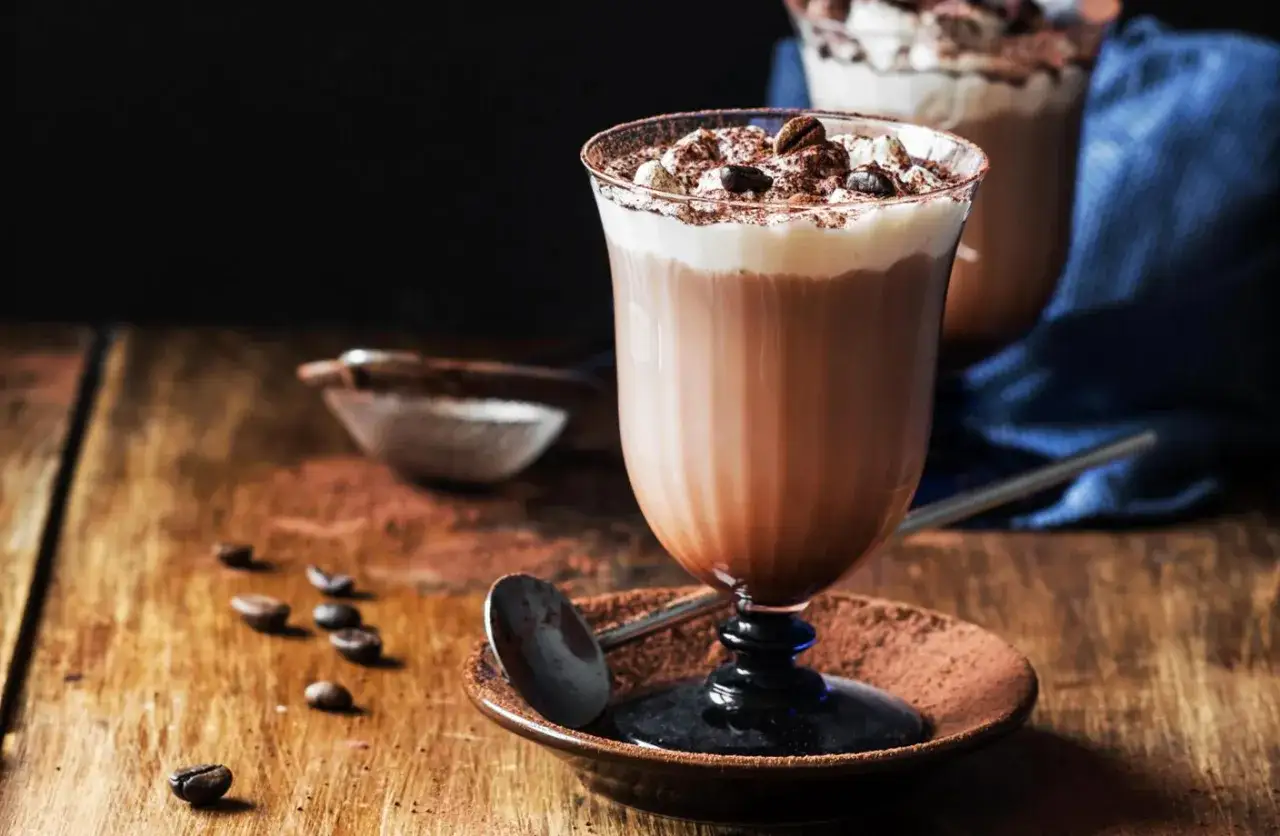 Ein k&ouml;stliches Frappuccino Rezept: Schokoladengetr&auml;nk mit Sahne, Kakaopulver und Kaffeebohnen garniert, auf einem Holztisch.