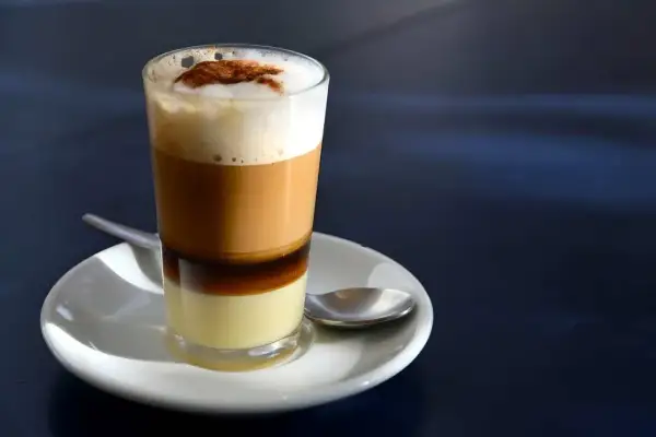 Ein geschichteter Kaffee mit Kondensmilch, Espresso und Milchschaum, bestreut mit Zimt. Ein süßer Genuss, wie ein flüssiger bonbon kaffee.