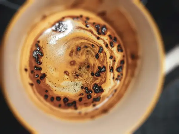 Nahaufnahme einer Tasse Kaffee mit Crema und Kaffeepulver, die an die Herstellung von Instantkaffee erinnert.