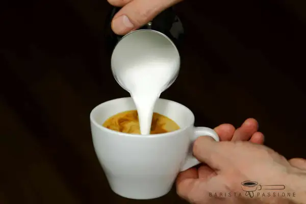 Milch wird in einen Espresso gegossen, um einen perfekten Espresso macchiato zu kreieren.