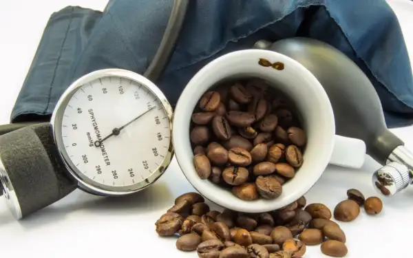 Blutdruckmessgerät und Kaffeebohnen. Die Frage, ob Kaffee senkt den Blutdruck, wird hier visuell thematisiert.