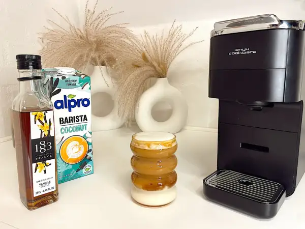 Ein leckerer Kokosnuss-Latte mit Alpro Barista Coconut, Vanillesirup und einer Kaffeemaschine.
