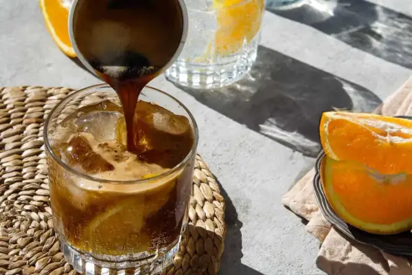 Espresso wird in ein Glas mit Eis und Orangenscheiben gegossen. Ein erfrischender Espresso Tonic für heiße Tage.