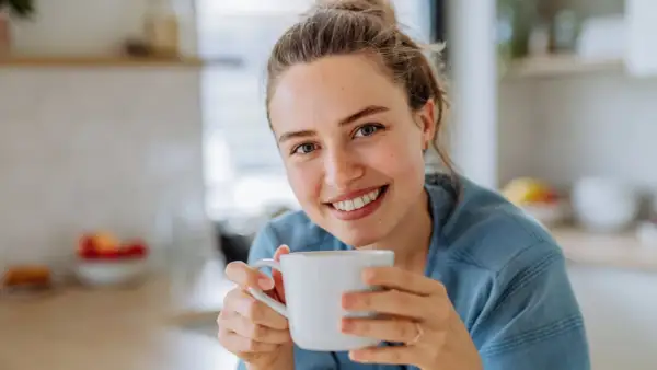 Lächelnde Frau hält eine Tasse Kaffee. Sie genießt den Moment, vielleicht trinkt sie alten Kaffee, um den Tag zu beginnen.