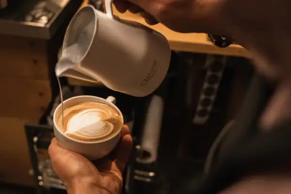 Barista kreiert ein Herz-Latte-Art-Muster, indem er Milchschaum in Kaffee gießt.
