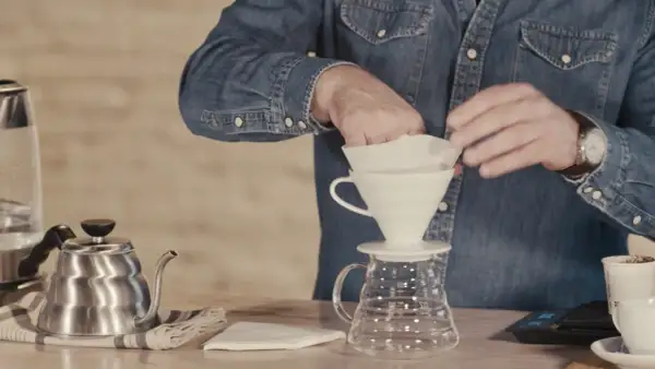 Mann bereitet sich auf das Kaffee filtern vor, indem er den Papierfilter in den Trichter legt.