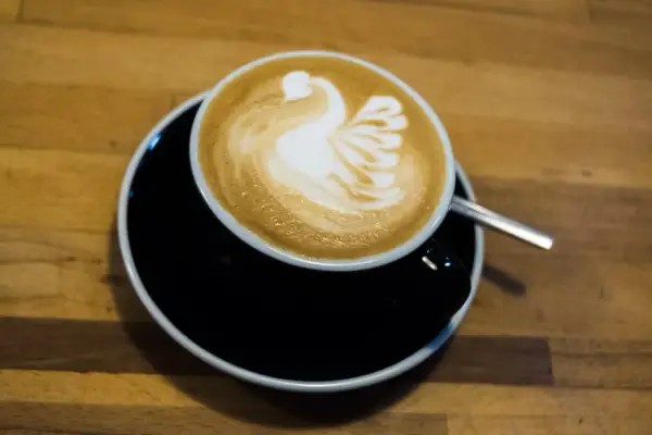 Kaffee mit einem Schwan aus Milchschaum zubereitet, serviert auf einem schwarzen Unterteller.
