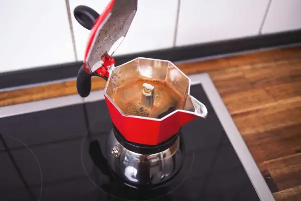 Roter Espressokocher auf dem Herd, der frischen Kaffee zubereitet. Der Duft von heißem Kaffee liegt in der Luft.