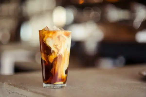 Ein Glas mit Eiswürfeln und cremiger Milch, die sich in dunklem Kaffee wirbelt. Perfekt für alle, die **cold brew selber machen** wollen.