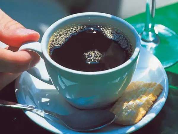 Eine Tasse schwarzer Kaffee mit Schaum, ein Keks und eine Löffel. So einfach ist, wie man schwarzen Kaffee macht.