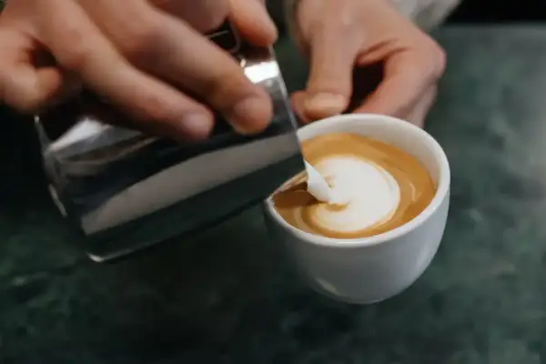 Barista gießt Milch in Kaffee, um ein Latte Art Herz zu kreieren.