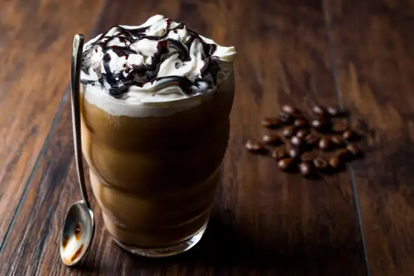 Eisgekühlter Kaffee mit Sahne und Schokoladensauce, ein köstliches Frappuccino Rezept. Daneben liegen geröstete Kaffeebohnen.