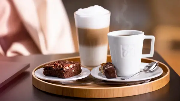 Ein Genussmoment: Dampfender Kaffee, ein Schoko-Brownie und ein Latte Macchiato, der zeigt, was ist cappuccino.