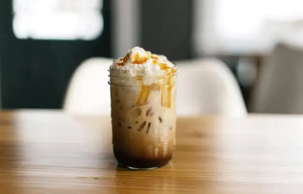 Ein köstlicher Caramel Frappuccino mit Sahne und Karamellsauce, serviert in einem Glas auf einem Holztisch.