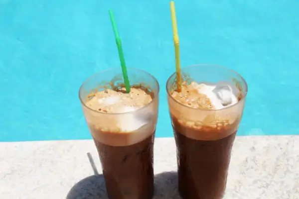 Zwei erfrischende Cafe Frappe mit Eis und Schaum stehen am Poolrand.
