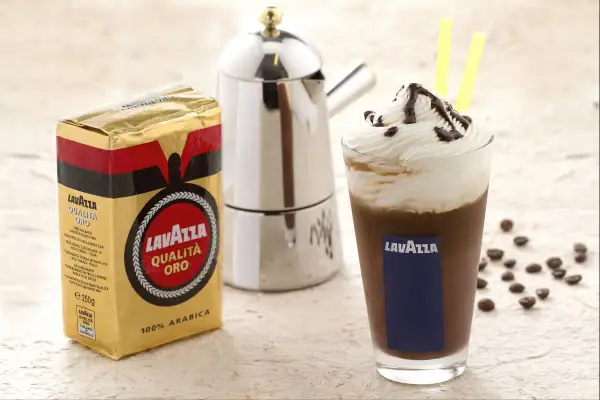 Ein köstlicher iced mocha mit Sahne und Schokoladensauce, daneben eine Packung Lavazza Qualità Oro Kaffee und eine Mokkakanne.