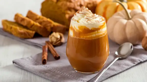 Ein cremiger Pumpkin Spice Latte mit Sahne und Zimt, daneben Kürbisbrot und Zimtstangen. Ein Genuss, der die pumpkin spice latte kalorien vergessen lässt.