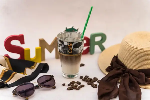 Ein erfrischender Vanilla Iced Coffee steht bereit für einen sonnigen Sommertag, umgeben von bunten Buchstaben, einer Sonnenbrille und einem Strohhut.