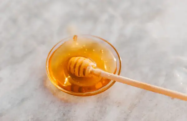 Ein Honiglöffel in einer Schale mit flüssigem Honig, der an den süßen Geschmack von Honey Process Kaffee erinnert.