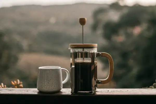 Eine French Press, bereit für den perfekten Kaffee. Neben einer Tasse wartet sie auf den Genuss.