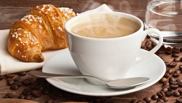 Dampfender Cappuccino mit Croissant und Kaffeebohnen. Ein Genuss, der die **Cappuccino Kalorien** wert ist.