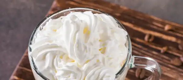 Ein Glas mit cremigem Cappuccino con panna, bedeckt mit einer üppigen Haube aus Schlagsahne.
