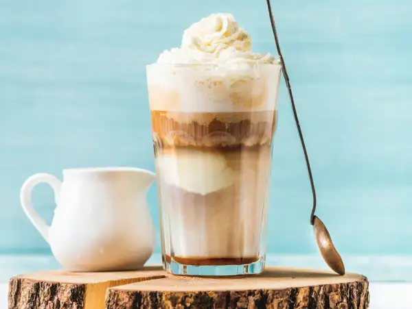 Ein cremiger Eiskaffee Karamell mit Sahnehaube, daneben ein Milchkännchen.